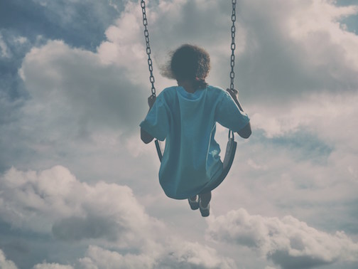 Young woman in a blue shirt swinging on a swingset. 